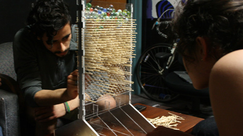 Two people staring at a rack with wooden sticks and marbles on top.