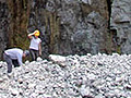 A photo of two people examining rocky ground in front of a massive cliff-face.