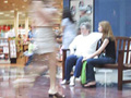 A photo of people sitting at a mall bench with people walking by.