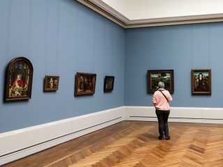 A person stands alone in a museum gallery, looking at paintings.