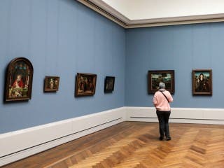A person stands alone in a museum gallery, looking at paintings.