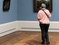 A person stands alone in a museum gallery, looking at paintings.