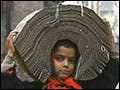 A young boy in India walks while carrying a tied up bundle of punched-data cards on his head.