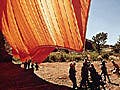 A tremendous orange cloth being hoisted into the air by teams of workers.
