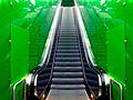 A photo of an escalator with green walls.