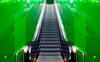 A photo of an escalator with green walls.