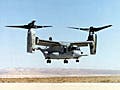 A photo of an CV-22 Osprey in rotorcraft mode, hovering above the ground.