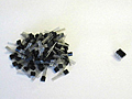 Photograph of a pile of 100 tiny discrete transistors next to an equally tiny 100 integrated transistors which are a single piece.