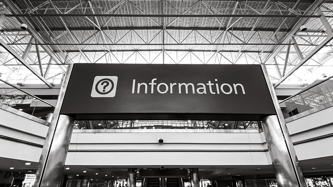 Black and white image of an information desk sign in a public place. 
