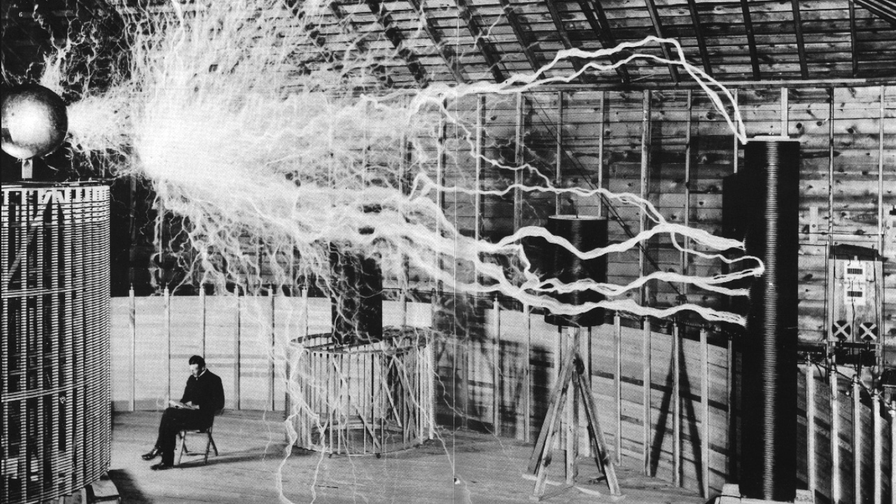 Black and white double-exposure photograph of Nikola Tesla in his laboratory with his coil in use.