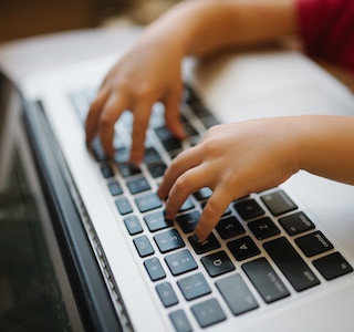 Child's hands typing at a laptop.