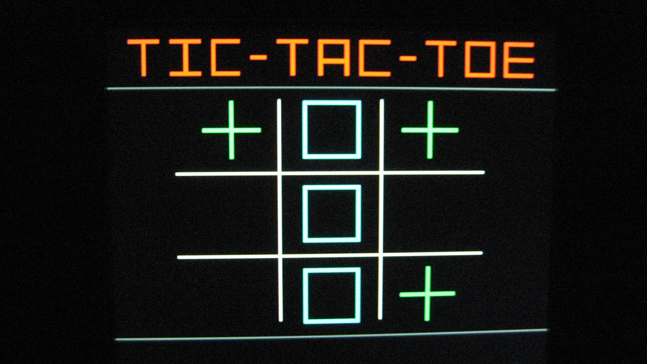 A digital screen displays a game of Tic-Tac-Toe. The board shows three green plus signs and three empty blue squares, with the title "TIC-TAC-TOE" at the top.