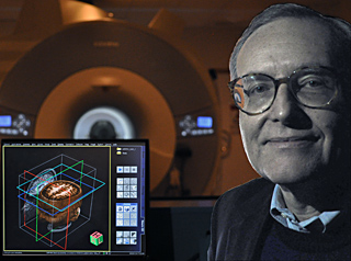 Photo of Professor Gabrieli sitting next to a computer display of human brain images, with fMRI scanner in the background.