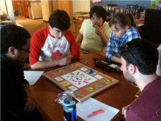 Five students sit around a table, playing a board game.