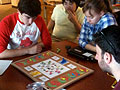 Five students sit around a table, playing a board game.