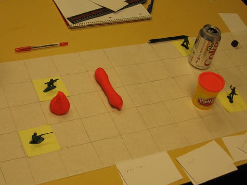 A grid on white paper contains a Diet Coke can, a Play-Doh tub, a large blob and a sausage of pink Play-Doh scattered about.