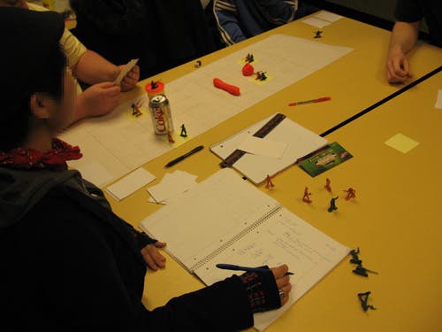 A student writes in a notebook while the game is played.