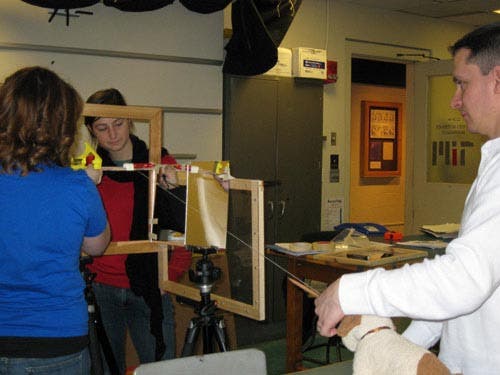 Photo of students looking through the perpendicularly arranged wooden frames at a stuffed dog, a string indicating line-of-sight.