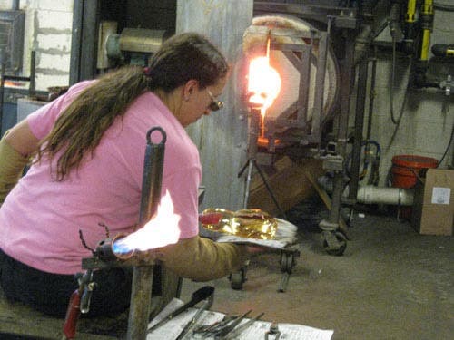 Photo of a glassblower working with hot glass.