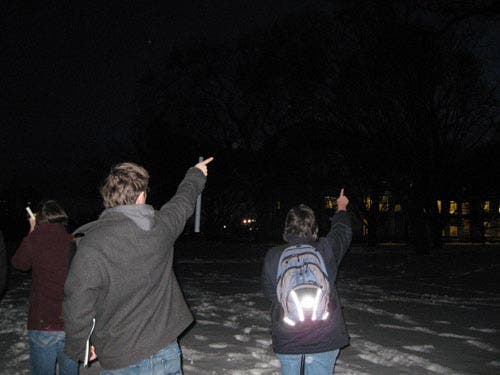 Photo of students pointing at an unseen object in the night sky.