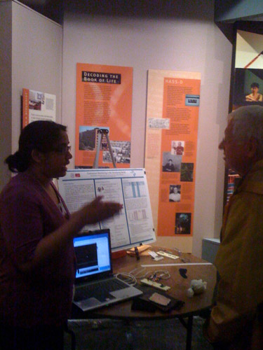 A photo showing a team member speaking with an attendee with poster and prototype nearby.