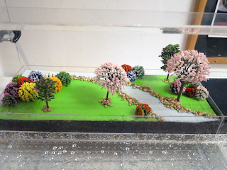Diorama of a grassy park and trees with water in front.