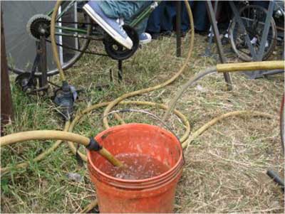 Close-up from prior photo showing water being pumped from a bucket through a long hose.