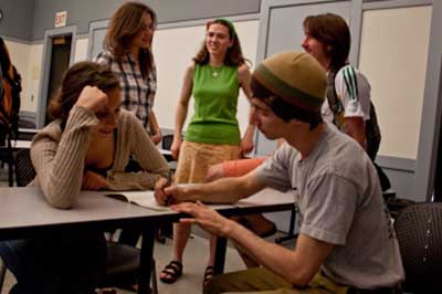 Shawn Frayne writing in a notebook while some students look on.