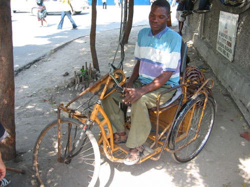 Photo of a person sitting in a trike by the side of road.