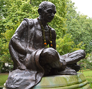 A statue of an elderly gentleman, with his head bowed and his legs crossed beneath him.