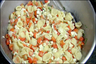 A bowl contains pasta shells, tomatoes, and cheese.