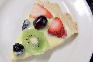 A slice of tart with berries and kiwi sits on a white plate.