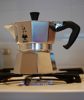 A silver metallic pitcher sits on top of the burner of a stove.