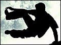 A photograph of the silhouette of a man vaulting over a wall set against a blue sky.
