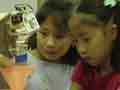 A photo of two girls creating a path for a falling ball on a peg board.