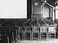 A black and white photo of movie hall with rows of wodden chairs.