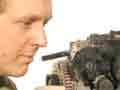 A man wearing a bluetooth earset is crouched next to an internal combustion engine.