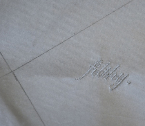 White embroidered fabric with the word ‘filthy’ in script.