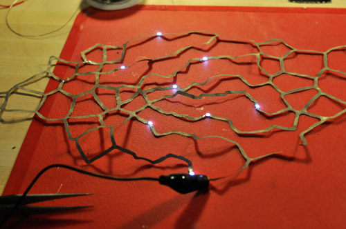 Photo of one of the laser cut fabric pieces, with several small white lights attached to branches.