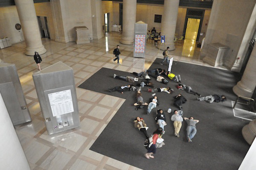 Photo of about 15 students lying on the floor of MIT’s Lobby 7, just inside a heavily-used doorway.