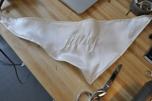 Photo of a triangular piece of white fabric, embroidered with the world ‘filthy’ in script.