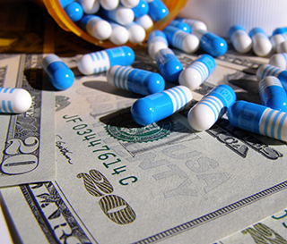 Blue and white tablets spilling out of a prescription bottle on top of a pile of crisp twenty dollar bills.