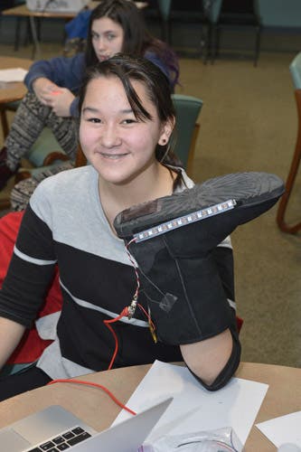 A girl holds a boot with wires attached.