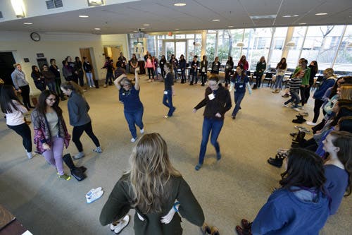 Several high school aged girls are standing in a large circle. A few girls are walking in the middle of the circle.