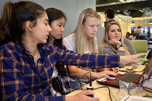 A photo of a group of girls working around a laptop.
