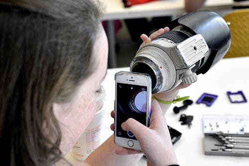 A photo of a girl using her iPhone camera to look through a telephoto lens.