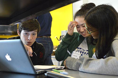 A photo of a workshop volunteer helping a group of girls working at a laptop.