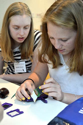 A photo of two girls taking apart a digital camera.