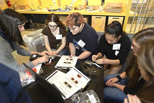 A group of girls sitting at a table, working on camera building.