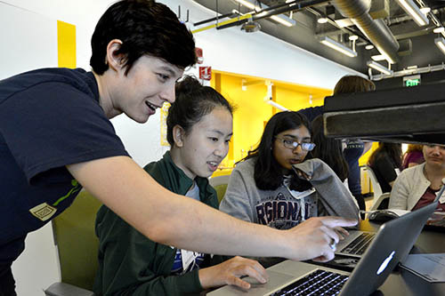 A photo of a workshop volunteer helping a group of girls working at a laptop.